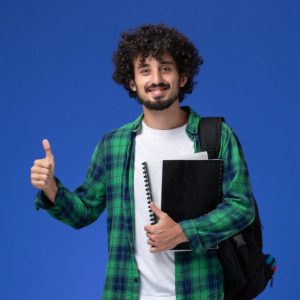front view male student in green checkered shirt with black backpack holding copybooks smiling on blue background university school college art drawing Student's review Med Edu Bishkek